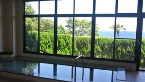 A room with a large window overlooking a lush garden and the sea.