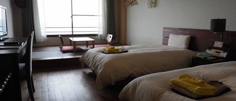 Une chambre d’hôtel avec deux lits, un bureau avec un ordinateur, une chaise et une fenêtre avec des rideaux.