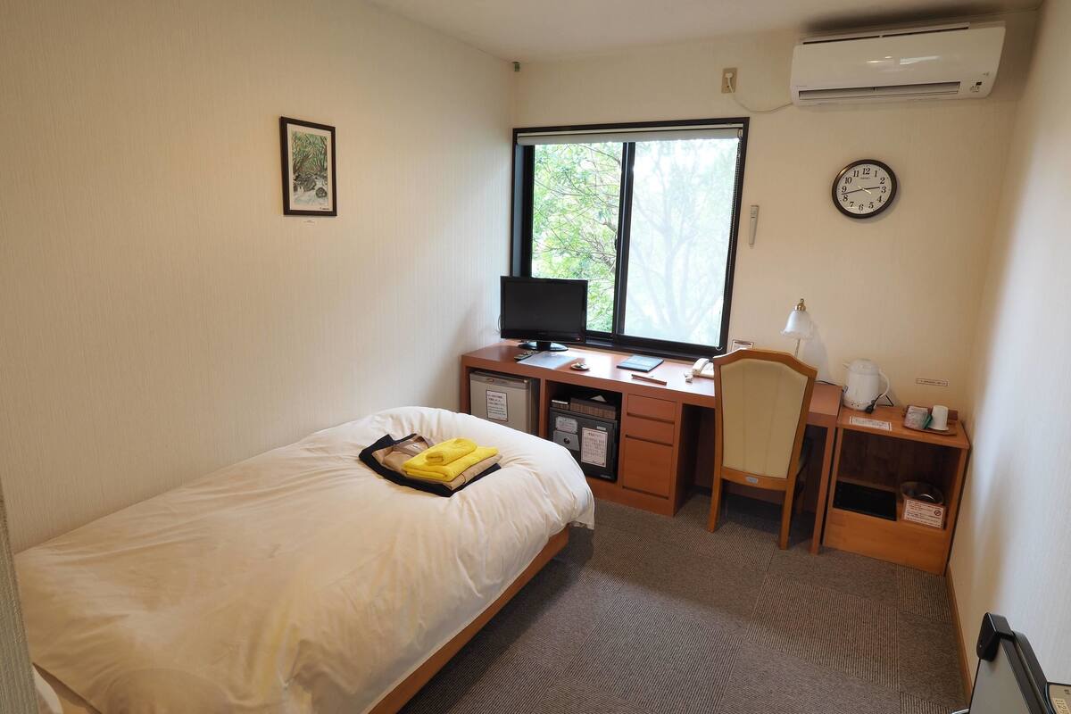 Une chambre d’hôtel équipée d’un lit, d’un bureau avec un ordinateur, d’une chaise, d’une horloge et d’un climatiseur.