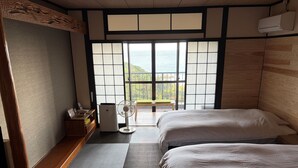 A traditional Japanese-style room with tatami flooring, two beds, a fan, and a view of the sea.