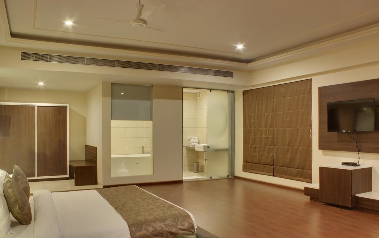 A modern hotel room with a large bed, a television mounted on the wall, and a sliding glass door leading to a bathroom.