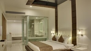 A modern hotel room with a large bed, a glass-enclosed shower, a bedside table with a phone, and a wall-mounted light. - Hotel Lakeview (Ahwa)
