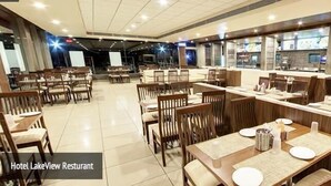 A restaurant with wooden tables and chairs, a counter with food displays, and a tiled floor. - Hotel Lakeview (Ahwa)