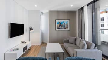 A modern living room with a flat-screen TV, a sofa, a coffee table, and a large window with a city view.