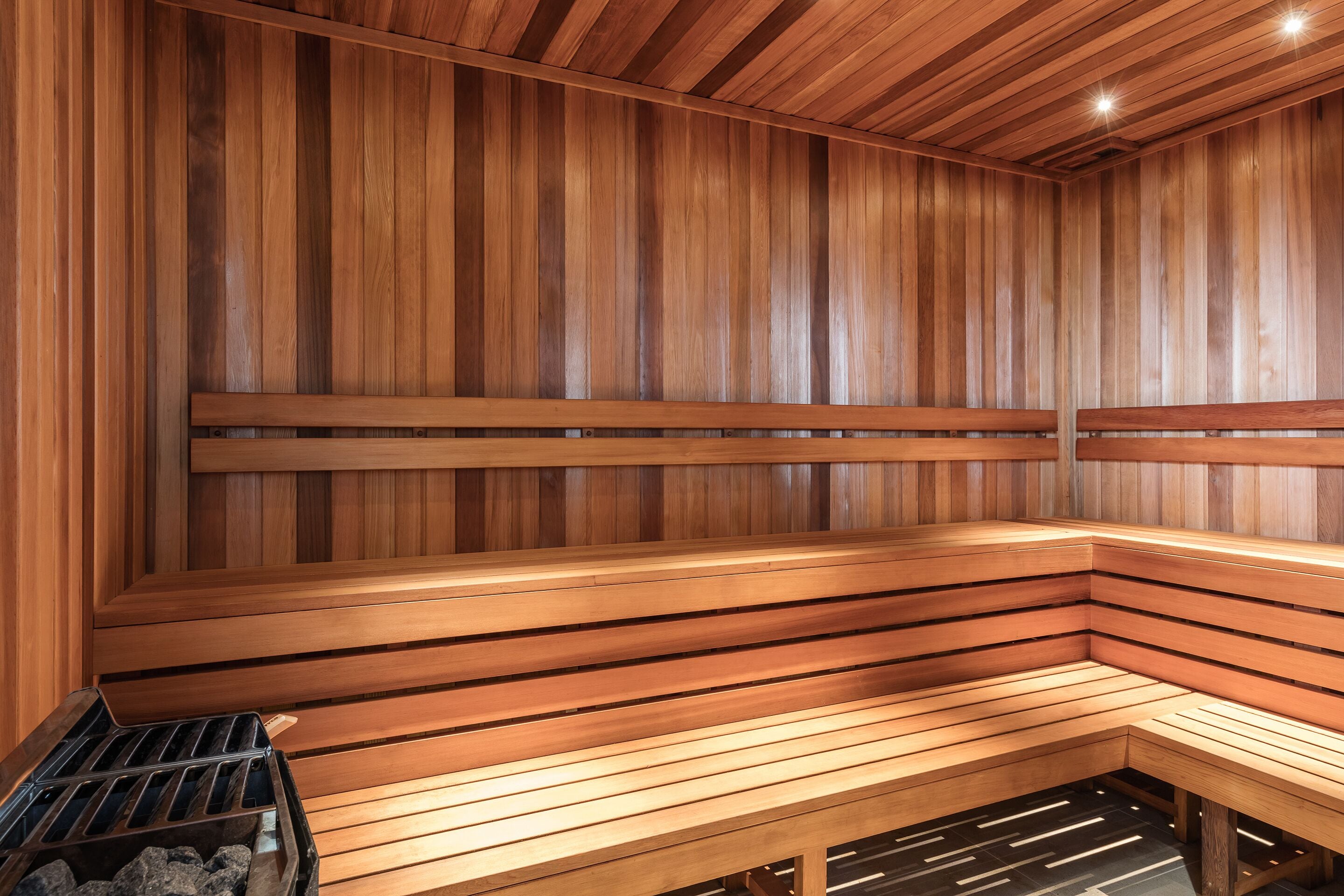 A sauna with wooden benches and a bench with a tray of rocks.