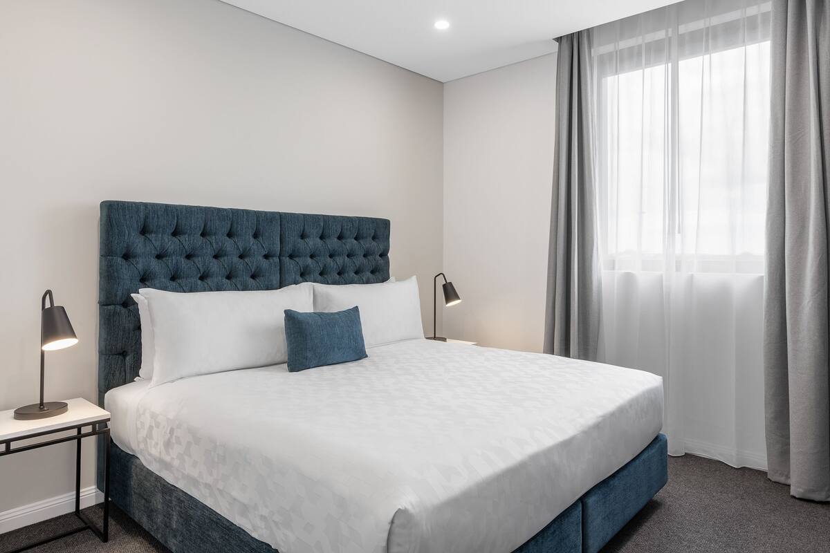 A neatly made bed with a tufted headboard, white bedding, and two bedside lamps.