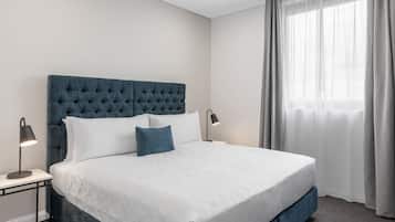 Cama bem arrumada com cabeceira estofada, roupa de cama branca e duas luminárias de cabeceira.