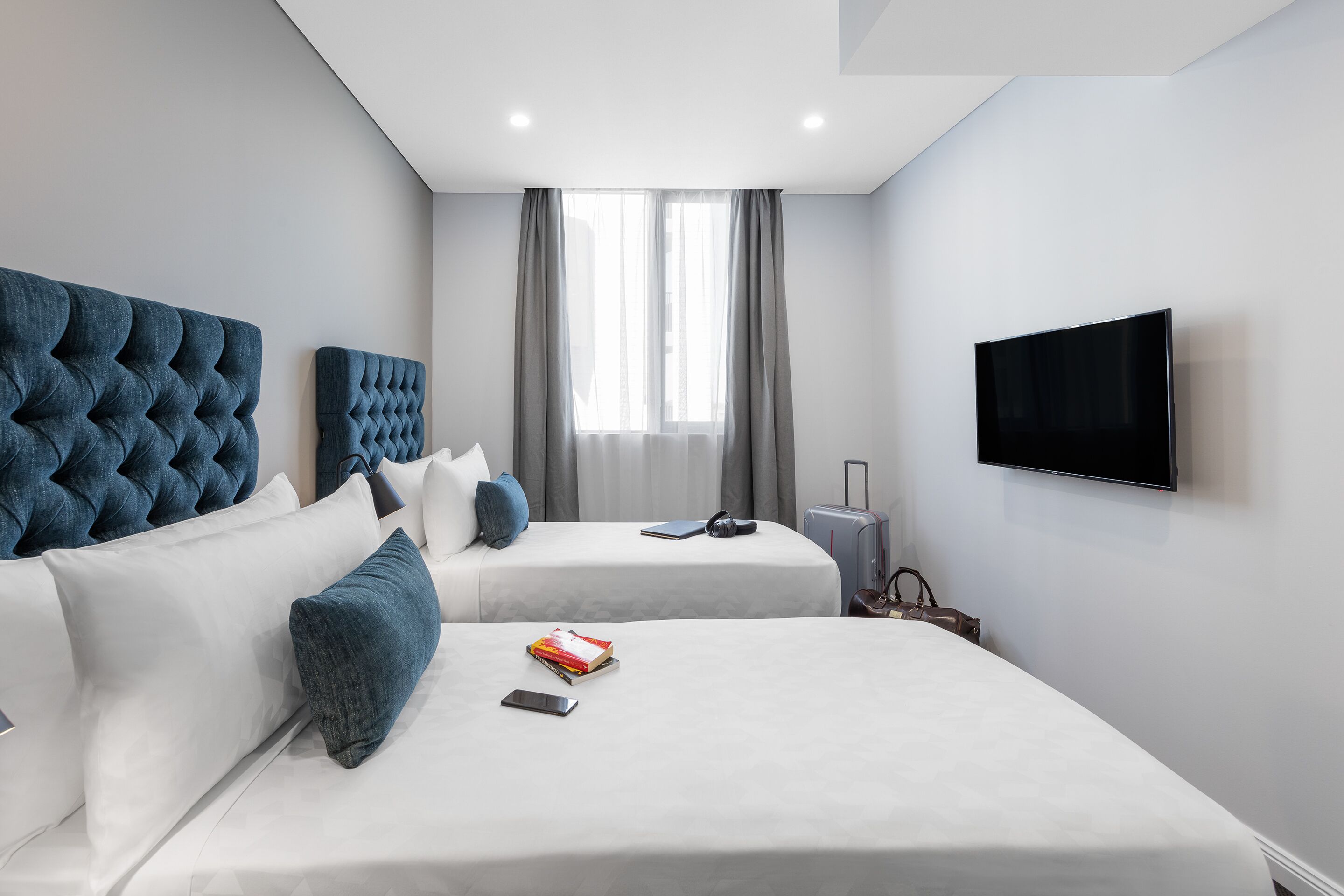 A modern hotel room with two beds, a flat-screen TV, and a window with curtains.