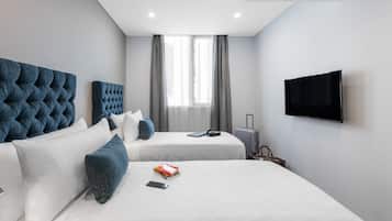 A modern hotel room with two beds, a flat-screen TV, and a window with curtains.