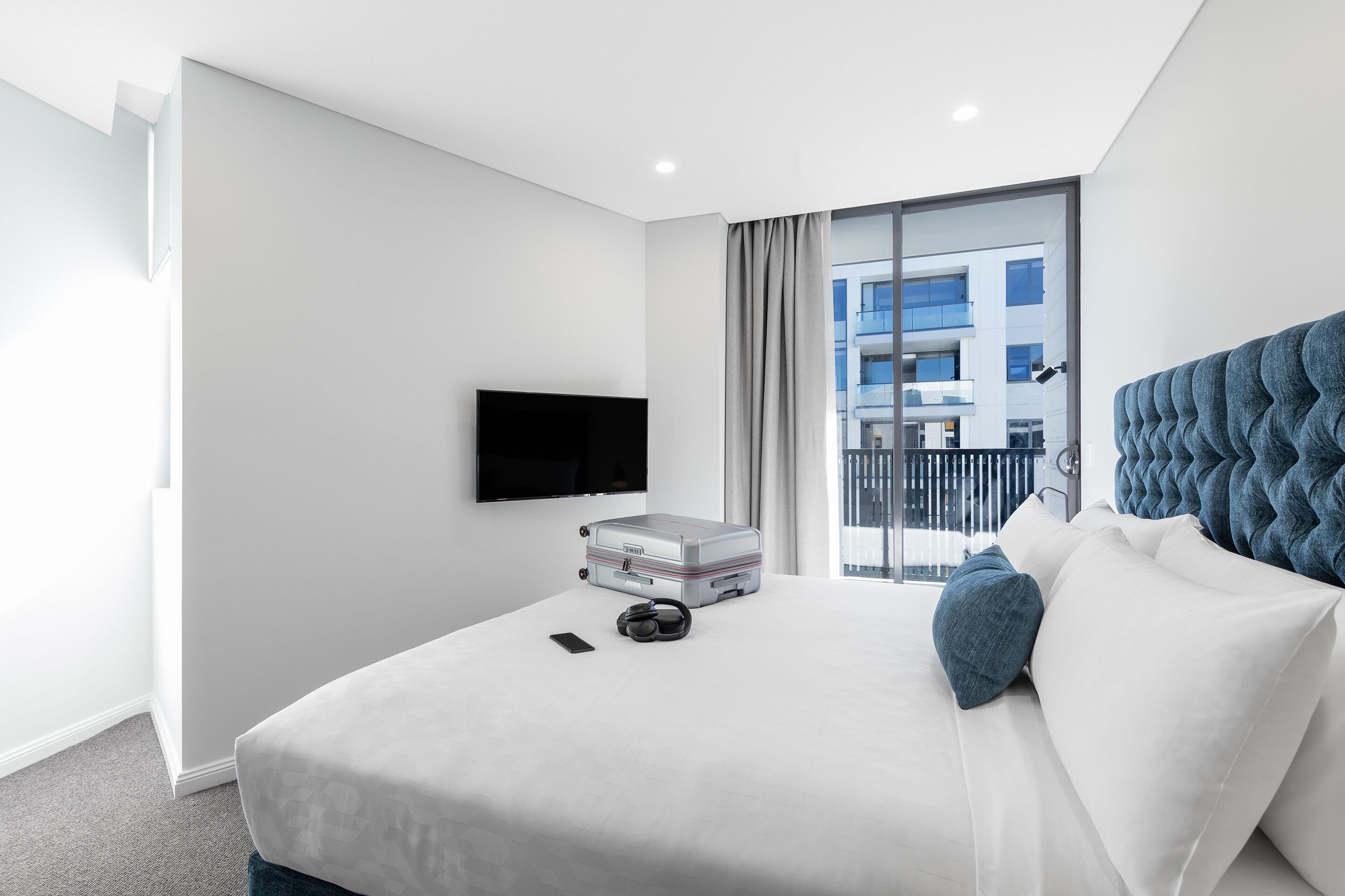 A modern hotel room with a large bed, a flat-screen TV mounted on the wall, and a view of the city through the window.