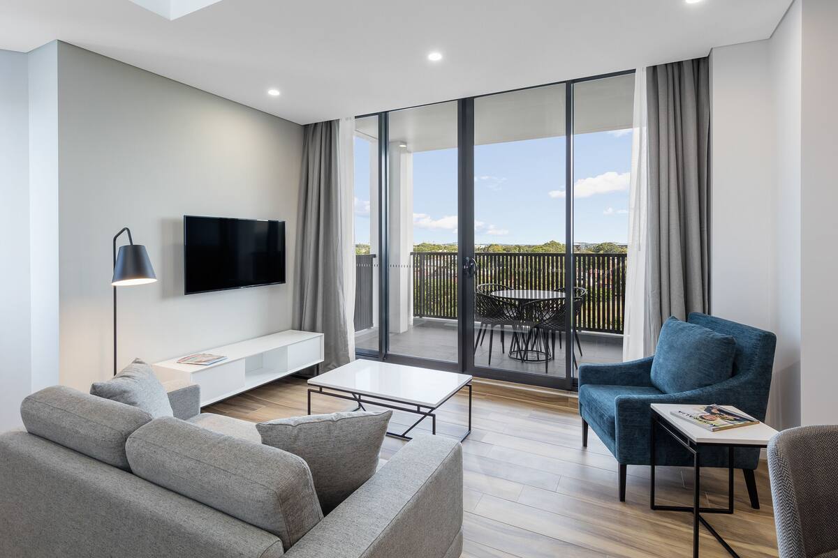 A modern living room with a grey sofa, a blue armchair, a coffee table, and a flat-screen TV mounted on the wall.