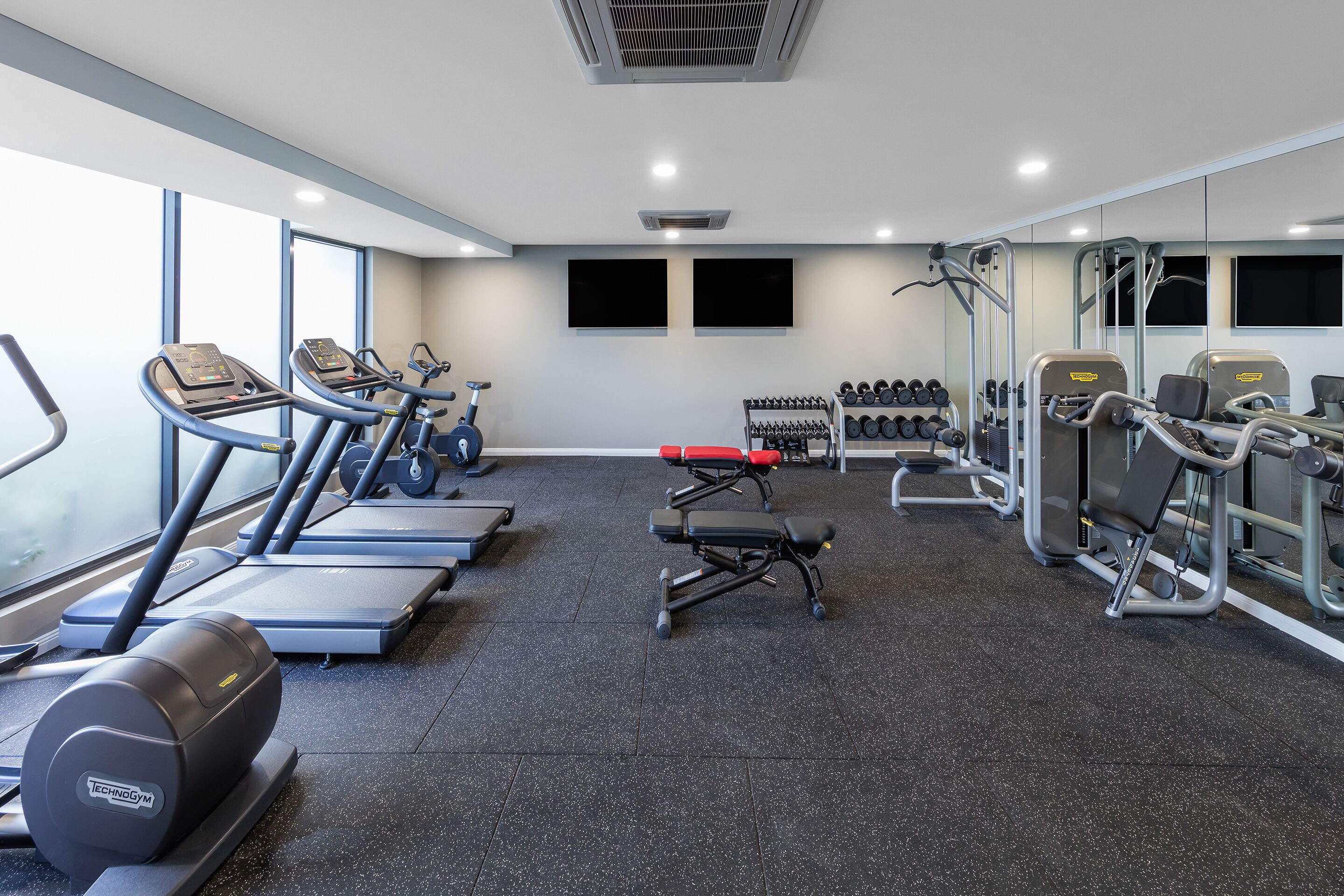 Een fitnessruimte met loopbanden, elliptische trainers, een bankdrukpers en gewichten.