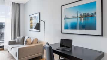 A modern hotel room with a grey sofa, a black desk with a laptop, and two framed pictures on the wall.