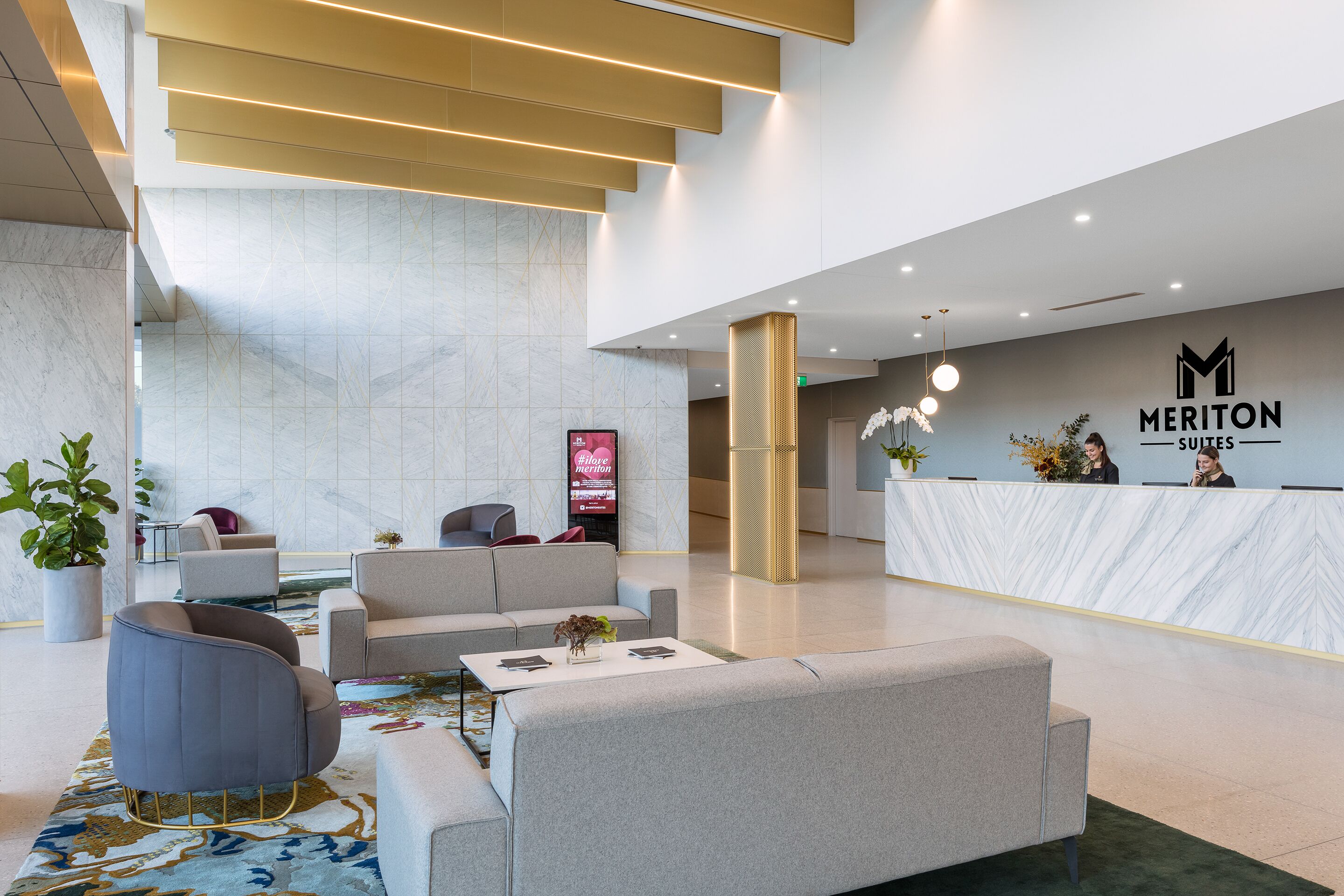 A modern hotel lobby with a reception desk, seating area, and a staircase.