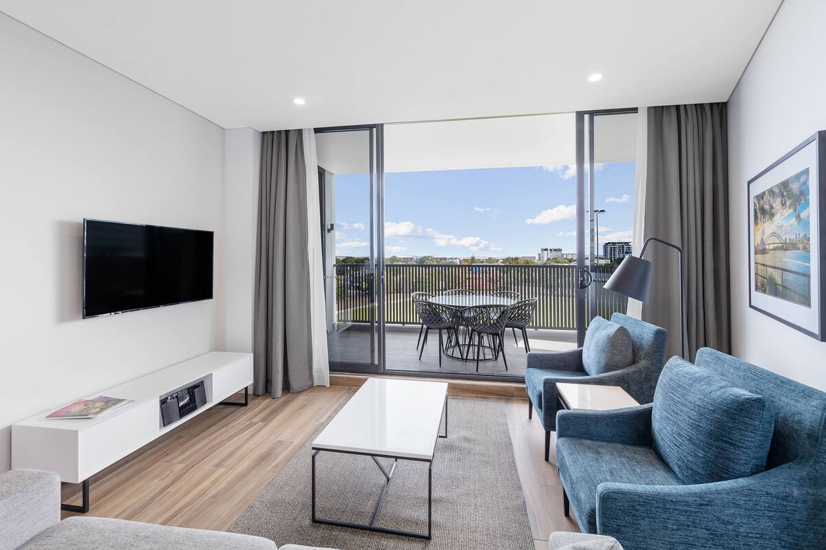 A modern living room with a flat-screen TV, a sofa, a coffee table, and a balcony with a table and chairs.