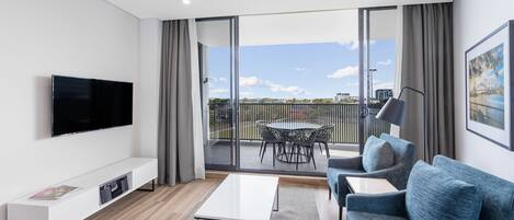 A modern living room with a flat-screen TV, a sofa, a coffee table, and a balcony with a table and chairs.