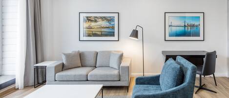 Ein modernes Wohnzimmer mit einem grauen Sofa, einem blauen Sessel, einem weißen Couchtisch, einer Stehlampe und zwei gerahmten Bildern an der Wand.