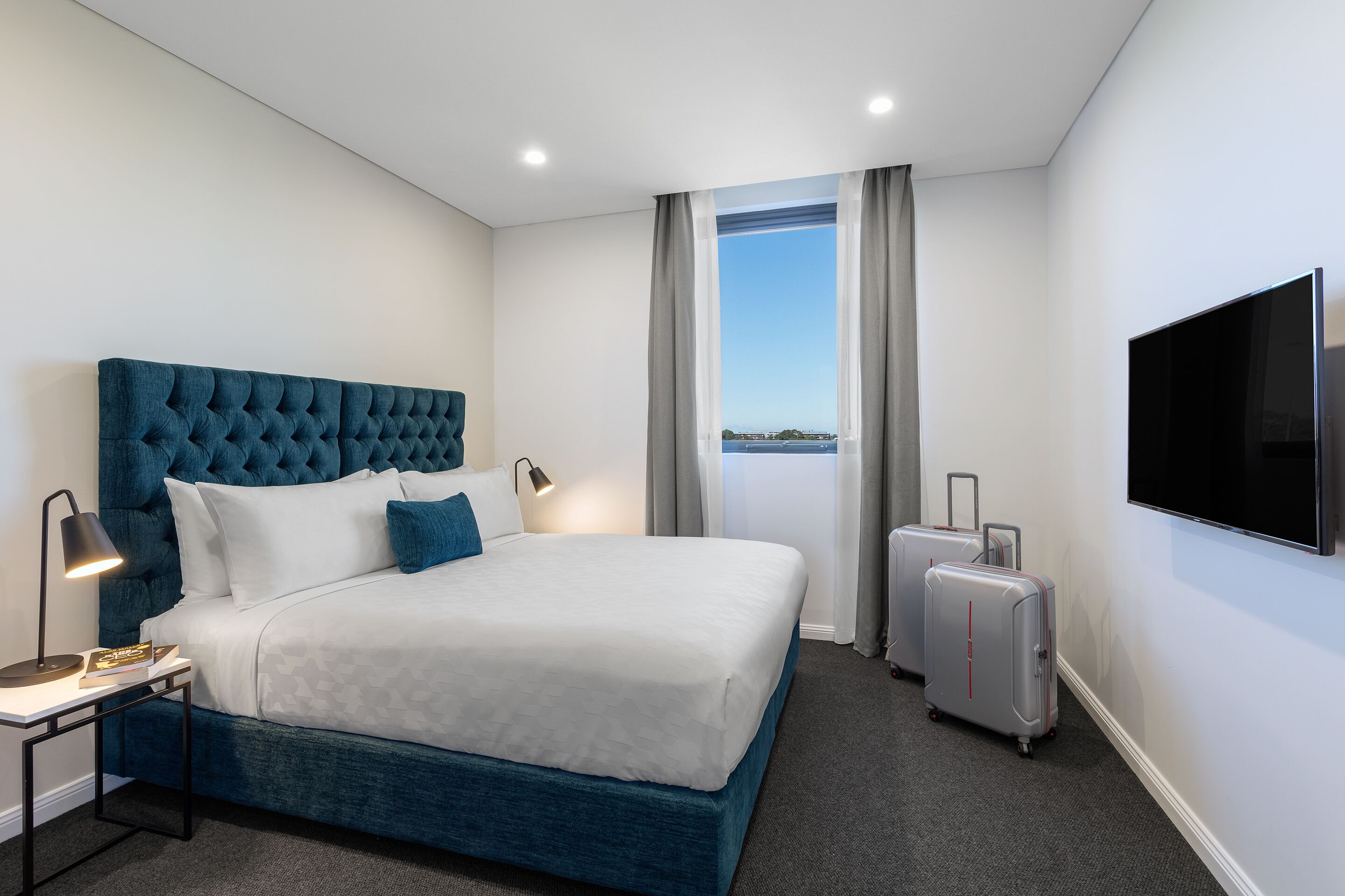 Habitación de hotel con una cama grande, un televisor de pantalla plana, un escritorio con lámpara y una maleta.
