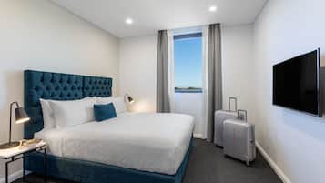 Habitación de hotel con una cama grande, un televisor de pantalla plana, un escritorio con lámpara y una maleta.