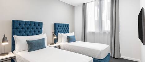 Une chambre d’hôtel avec deux lits, chacun doté d’une tête de lit bleue, de draps blancs et d’une lampe de chevet.