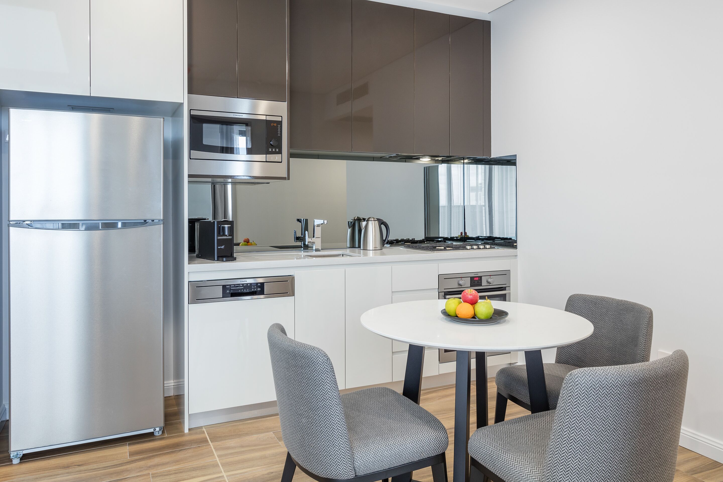 Una cocina moderna con electrodomésticos de acero inoxidable, una mesa de comedor blanca y sillas tapizadas en gris.