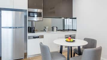 A modern kitchen with stainless steel appliances, a white dining table, and grey upholstered chairs.