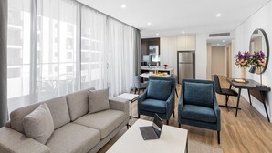 Un saló modern amb un sofà, dues butaques, una taula de centre i un ordinador portàtil. Hi ha una zona de menjador amb una taula i cadires, i una cuina al fons.
