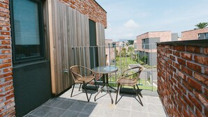 A balcony with two wicker chairs and a small round table, a wooden door, and a brick wall. - Jeju Daonjae (Seogwipo)