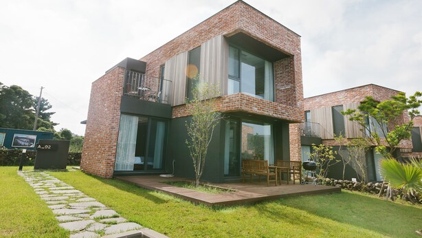 A modern two-story house with a brick facade, large windows, and a small patio area with outdoor furniture. - Jeju Daonjae (Seogwipo)