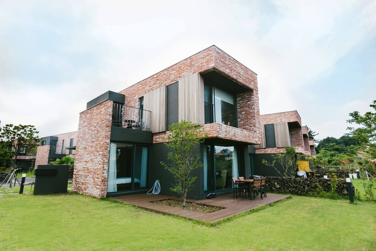 A modern two-story house with a brick exterior, large windows, and a small garden area with a table and chairs.