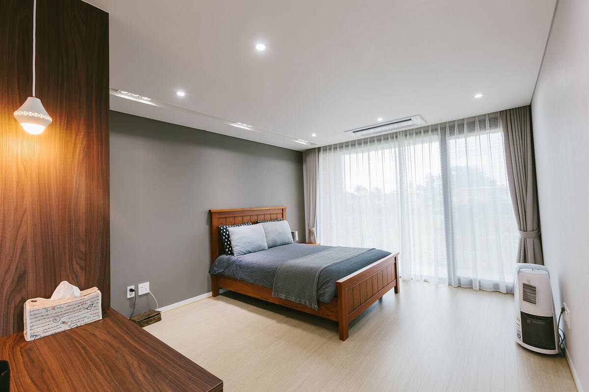 A modern bedroom with a wooden bed, a bedside table, a nightstand, and a wall-mounted heater.