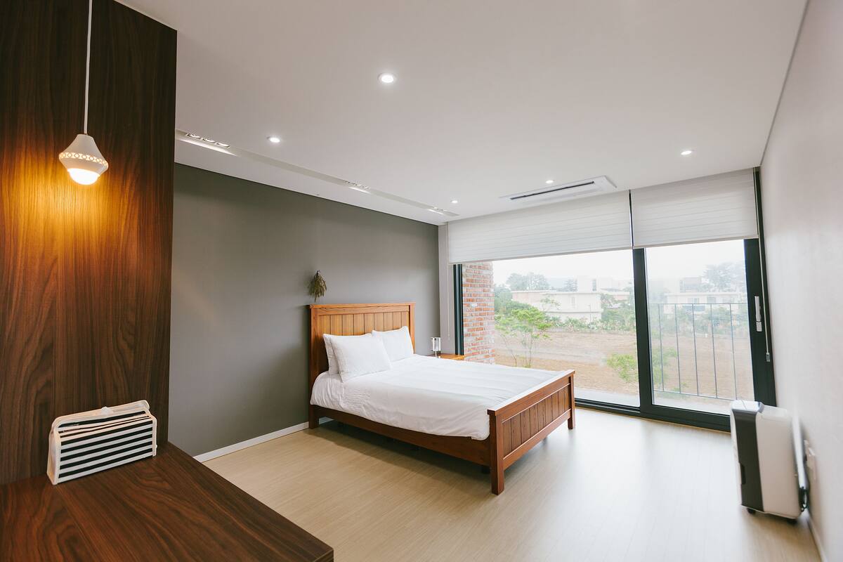 A modern bedroom with a wooden bed, a radiator, and a large window with a view.