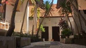 A courtyard with a tiled floor, palm trees, and a building with a tiled roof. - Padang Padang Breeze (Pecatu)