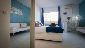 Ein Schlafzimmer mit einem Bett, einem Sofa, einem Sessel, einem Schreibtisch und einem Fenster mit Vorhängen.