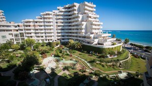Ein mehrstöckiges Hotel mit Balkonen, einem angelegten Garten mit Pools und Blick aufs Meer.