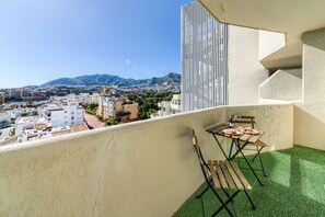 A balcony with a table and chairs, a view of a cityscape and mountains in the background.
