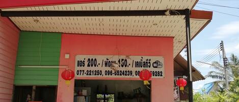 A storefront with a blue and red facade, featuring a sign with Thai script and contact numbers.