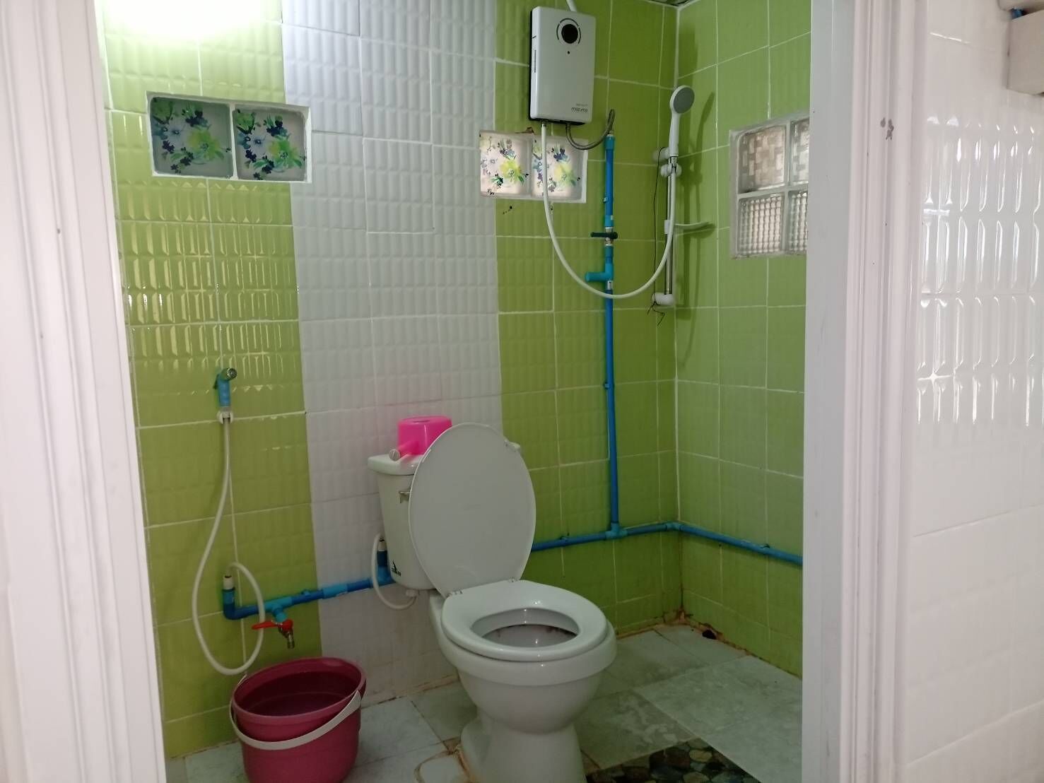 Un baño con baldosas verdes y blancas, un inodoro, una ducha y un cubo.