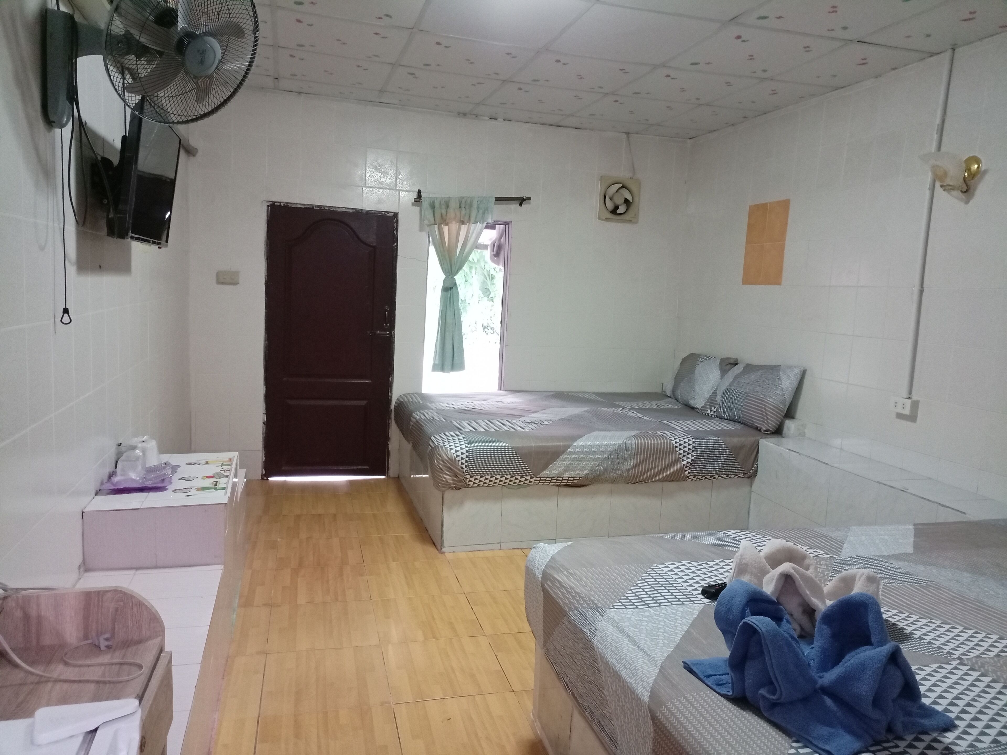 A room with a bed, a bedside table, a fan, and a window with curtains.