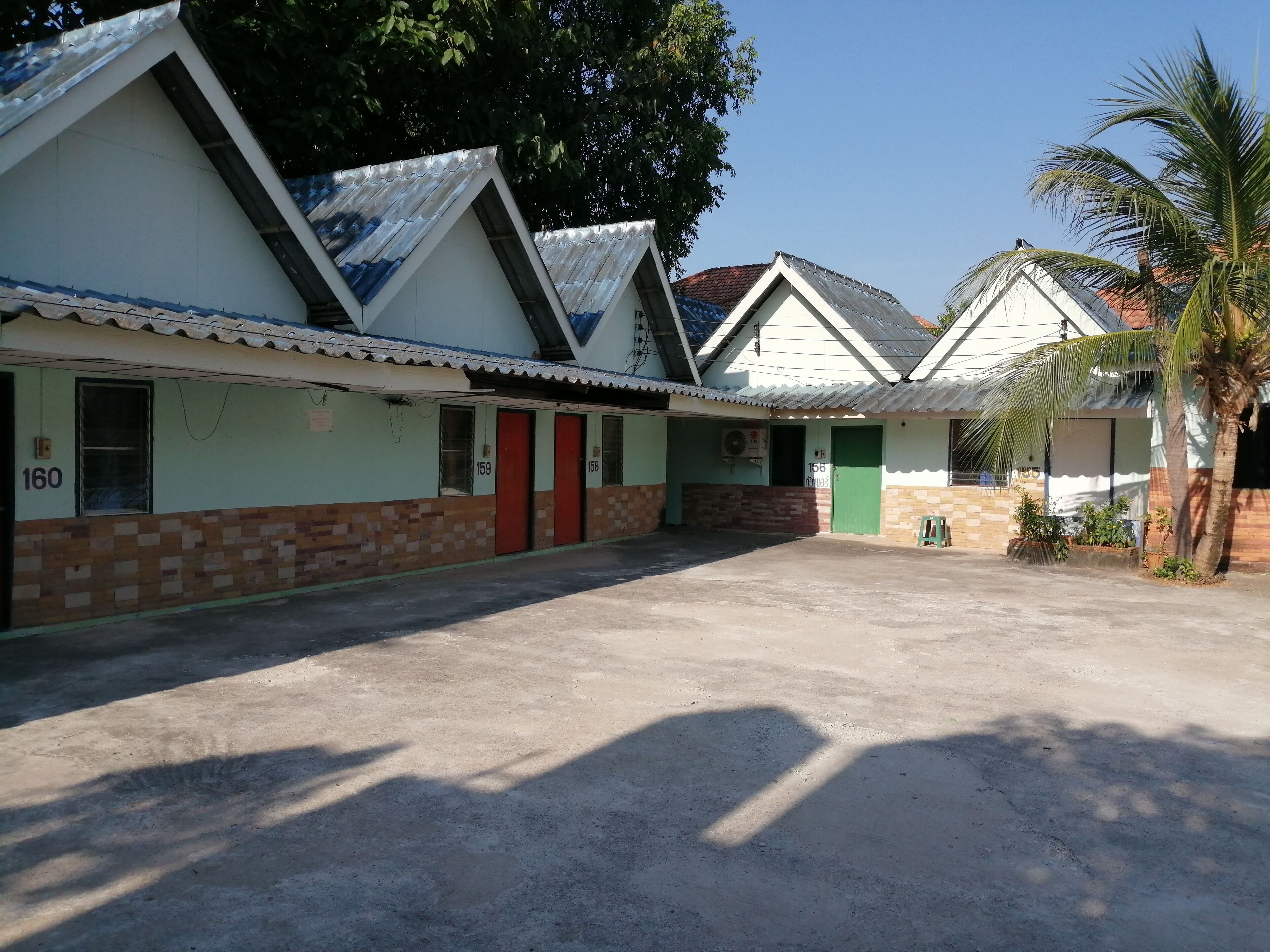 A row of simple, single-story buildings with numbered doors, a concrete courtyard, and a palm tree.