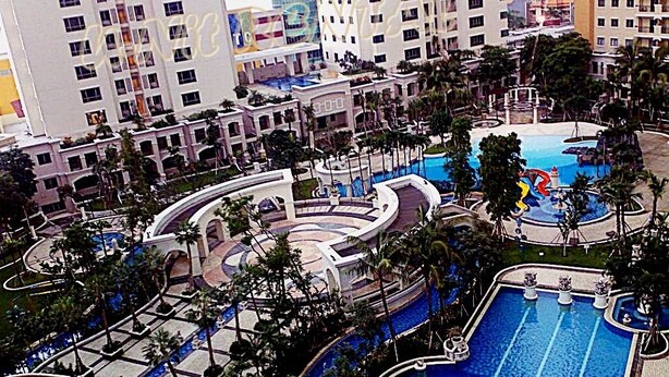 A resort with multiple swimming pools, palm trees, and high-rise buildings in the background. - Waterplace Residence (Surabaya)