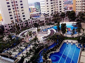 A resort with multiple swimming pools, palm trees, and high-rise buildings in the background. - Waterplace Residence (Surabaya)