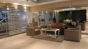 A modern living room with a sofa, armchairs, a coffee table, and a glass partition with blinds. - Waterplace Residence (Surabaya)