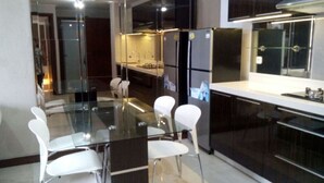 A modern kitchen with a glass dining table, white chairs, and dark cabinetry. - Waterplace Residence (Surabaya)