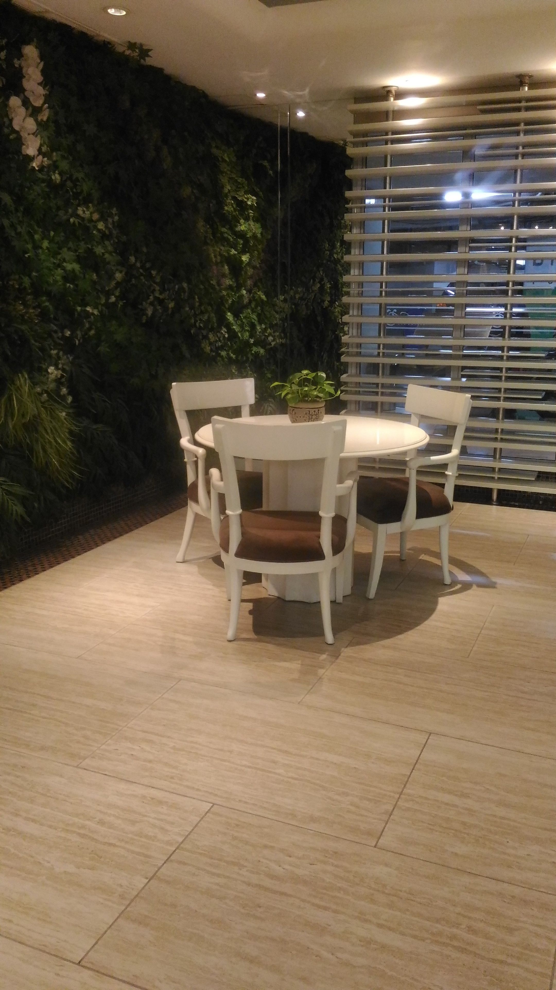 A dining area with a round table and four chairs, a potted plant on the table, and a wall with green foliage.