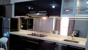 A modern kitchen with dark cabinets, a white countertop, a stainless steel sink, and a built-in oven. - Waterplace Residence (Surabaya)