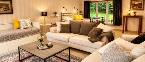 A well-lit living room with a sofa set, a coffee table, and a view of a garden through a sliding door.