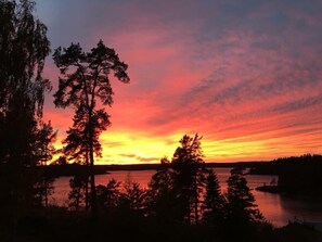 A sunset over a lake with trees silhouetted against the sky. - Vätternterrassen (Hammar)