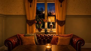 A cozy room with a leather sofa, a table with a candle, and a window with curtains.