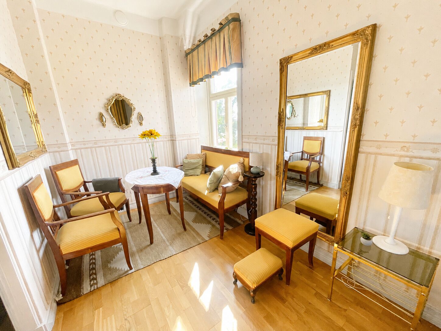 A room with a sofa, chairs, a table, a mirror, and a lamp.